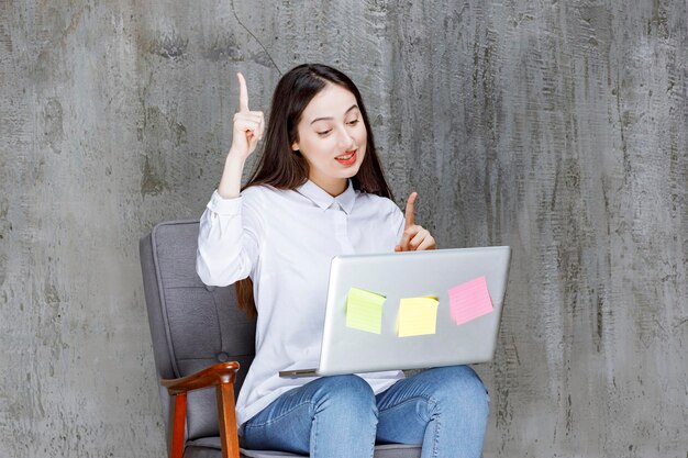 Jeune femme concentrée assise sur un fauteuil avec un ordinateur portable ayant une idée. Photo de haute qualité