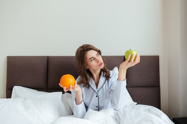 Jeune femme concentrée choisissant entre orange et pomme