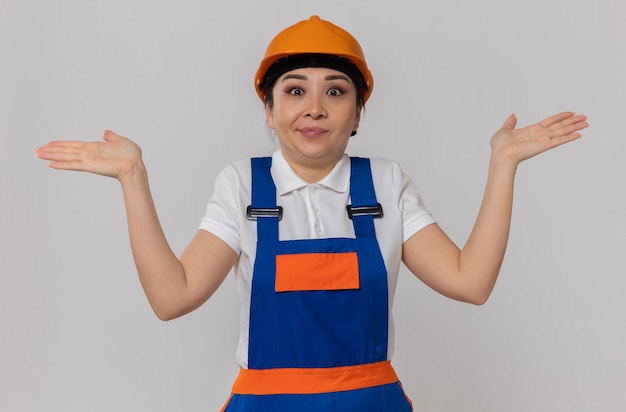 Jeune femme de constructeur asiatique confuse avec un casque de sécurité orange gardant les mains ouvertes