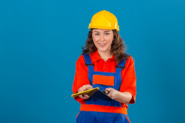 Photo gratuite jeune femme constructeur en uniforme de construction et casque de sécurité debout avec couteau à mastic souriant sympathique sur mur bleu isolé