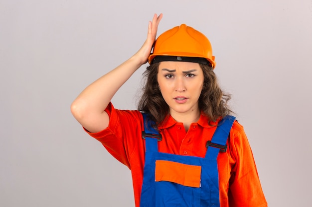 Photo gratuite jeune femme constructeur en uniforme de construction et casque de sécurité debout surpris avec la main sur la tête pour erreur mauvaise mémoire concept sur mur blanc isolé