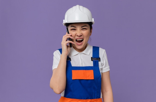 Jeune femme de construction asiatique agacée avec un casque de sécurité blanc criant sur quelqu'un au téléphone