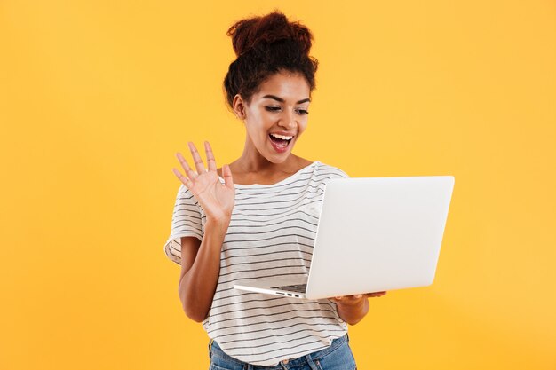 Jeune femme cool positive avec des cheveux bouclés à l'aide d'un ordinateur portable isolé