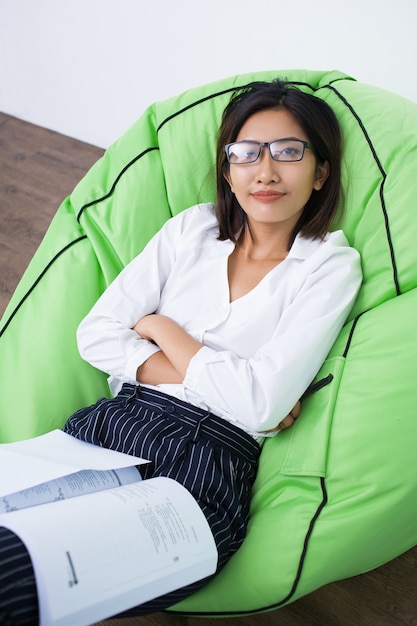 Jeune femme couchée dans le président Beanbag avec Magazine