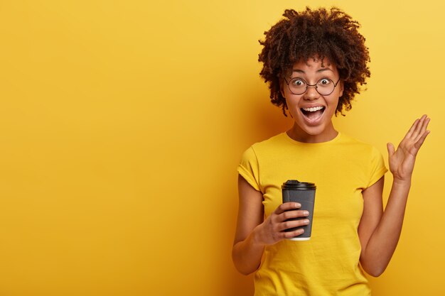 Jeune femme avec coupe de cheveux afro et T-shirt jaune tenant une tasse de café