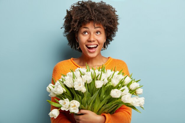 Jeune femme avec coupe de cheveux afro tenant un bouquet de fleurs blanches