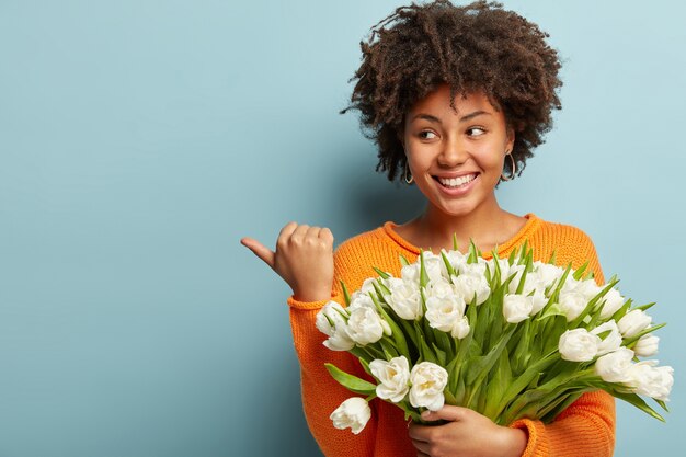 Jeune femme avec coupe de cheveux afro tenant un bouquet de fleurs blanches