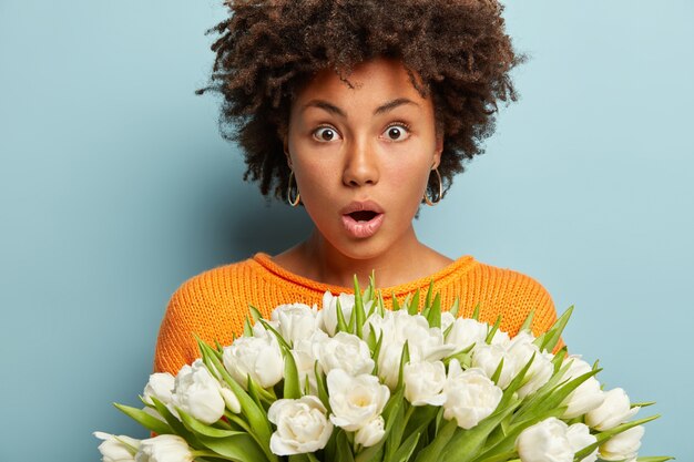 Jeune femme avec coupe de cheveux afro tenant un bouquet de fleurs blanches