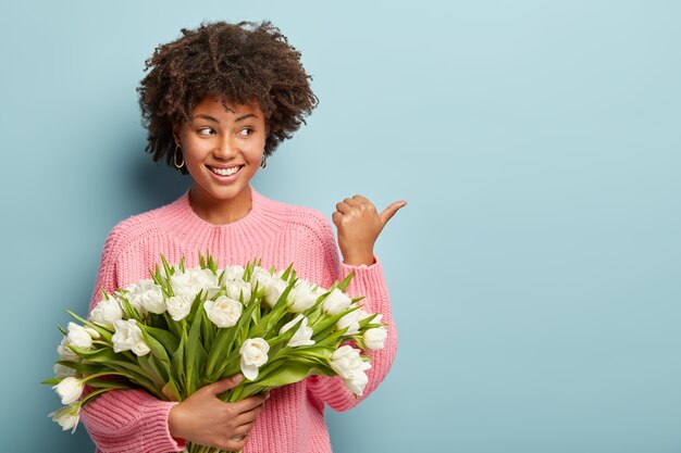 Jeune femme avec coupe de cheveux afro tenant un bouquet de fleurs blanches