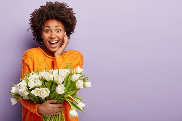 Jeune femme avec coupe de cheveux afro tenant un bouquet de fleurs blanches