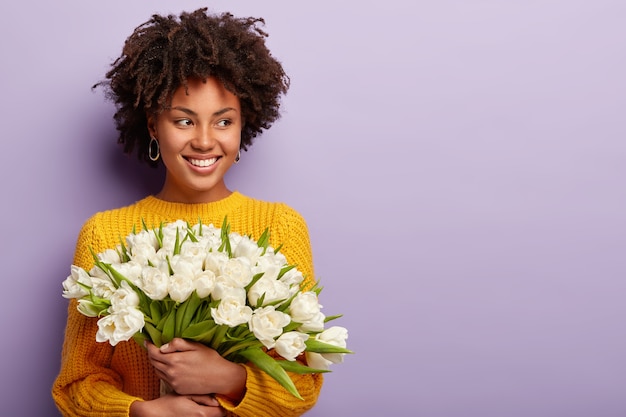 Jeune femme avec coupe de cheveux afro tenant un bouquet de fleurs blanches