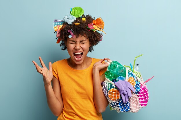 Jeune femme avec coupe de cheveux afro tenant un sac avec des déchets plastiques