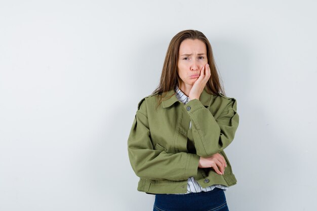 Jeune femme courbant les lèvres, debout dans une pose de réflexion en chemise, veste et regardant abattu. vue de face.