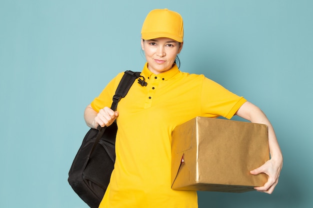 jeune femme courrier en jaune t-shirt capuchon jaune tenant la boîte sur le mur bleu