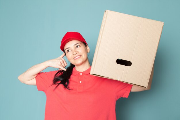 jeune femme courrier en rose t-shirt casquette rouge tenant la boîte sur le mur bleu