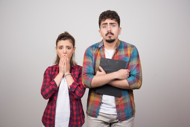 Une jeune femme couvrant la bouche et un homme tenant un presse-papiers.