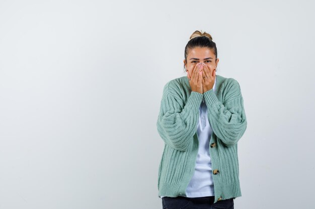 Jeune femme couvrant la bouche avec les mains en t-shirt blanc et cardigan vert menthe et à la surprise