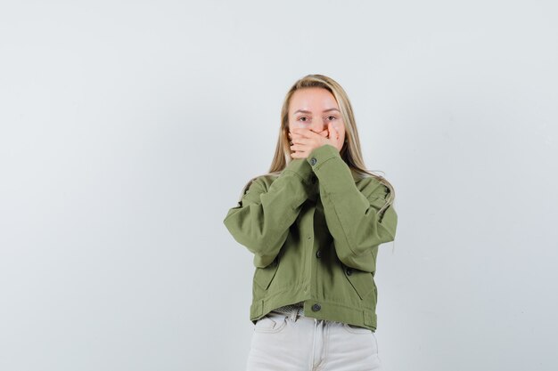 Jeune femme couvrant la bouche avec les mains en veste, chemisier et à la vue troublée, de face.