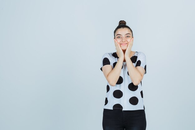 Jeune femme couvrant les joues avec les mains en t-shirt, jeans et à la jolie vue de face.