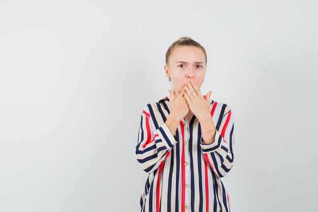 Jeune femme couvrant sa bouche avec les deux mains en chemisier rayé et à choqué