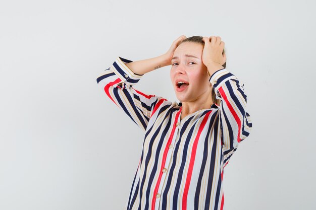 Jeune femme couvrant sa tête avec les deux mains en chemisier rayé et à épuisé