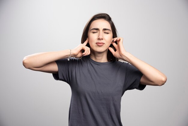 Jeune femme couvrant ses oreilles sur un fond gris.