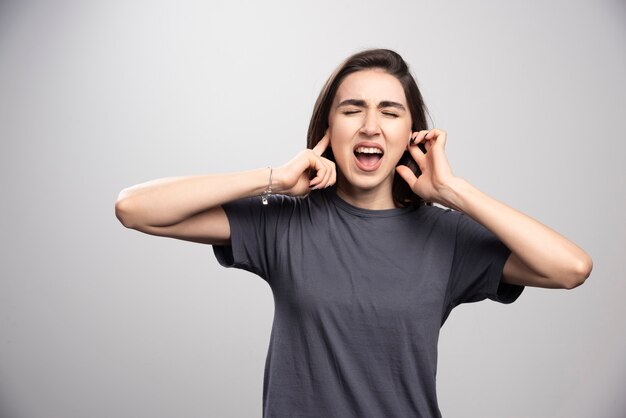 Jeune femme couvrant ses oreilles sur un fond gris.