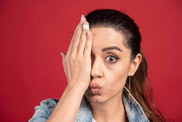 Jeune femme couvrant son œil à la main sur fond rouge. photo de haute qualité