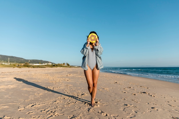 Jeune femme couvrant le visage avec assiette de frisbee sur la plage