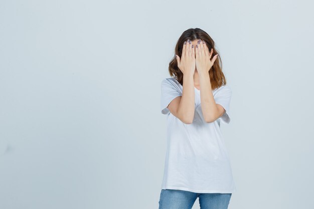 Jeune femme couvrant le visage avec les mains en t-shirt, jeans et à la recherche de sérieux. vue de face.