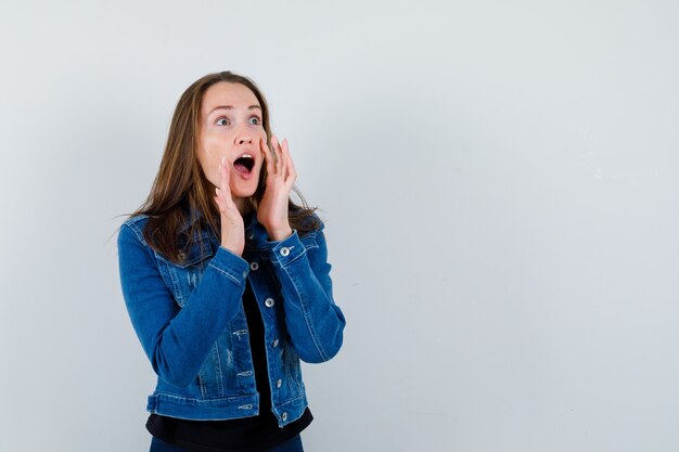 Jeune femme criant ou annonçant quelque chose en blouse, veste et semblant excitée, vue de face.