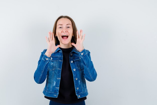 Jeune femme criant ou annonçant quelque chose en blouse, veste et semblant heureuse, vue de face.