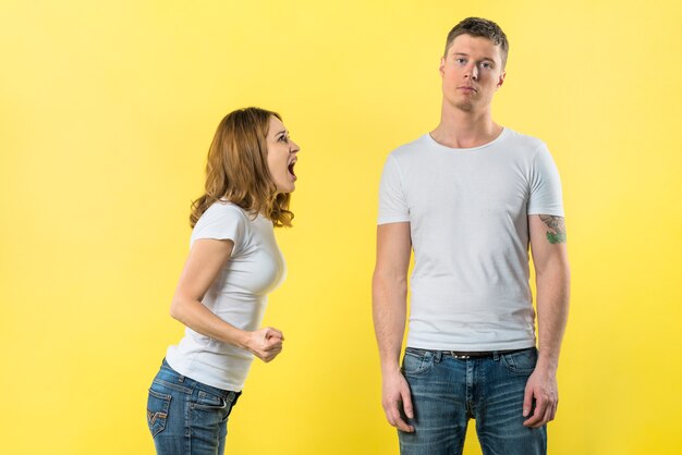 Jeune femme criant sur son petit ami debout sur fond jaune