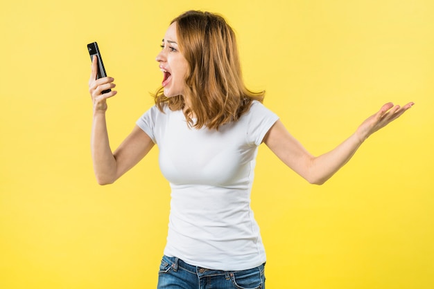 Jeune femme crier au téléphone intelligent sur fond jaune