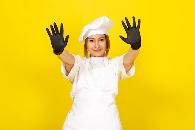 Jeune femme cuisine en costume de cuisinier blanc et bonnet blanc en gants noirs