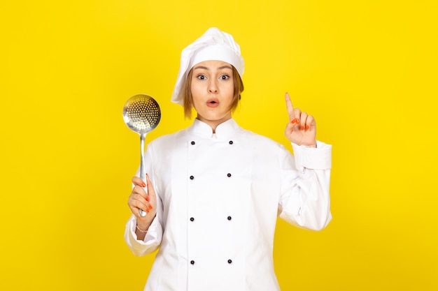 Jeune femme cuisine en costume de cuisinier blanc et bonnet blanc posant la pensée tenant une cuillère en argent ayant une idée