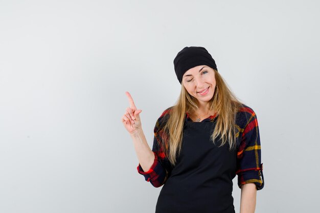 Jeune femme cuisinier dans un tablier noir pointant vers le haut