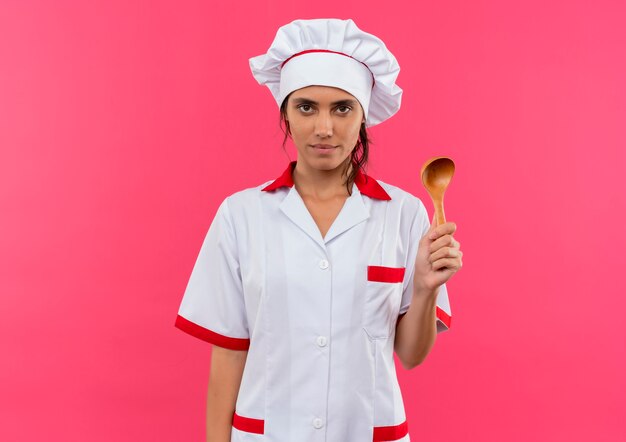 Jeune femme cuisinier portant un uniforme de chef tenant une cuillère sur un mur rose isolé avec copie espace