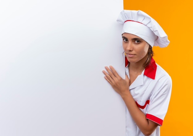 Photo gratuite jeune femme cuisinier portant l'uniforme de chef tenant un mur blanc sur un mur jaune isolé avec copie espace