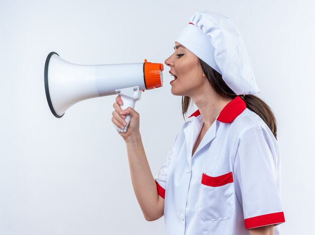 Jeune femme cuisinier en uniforme de chef parle sur haut-parleur isolé sur fond blanc