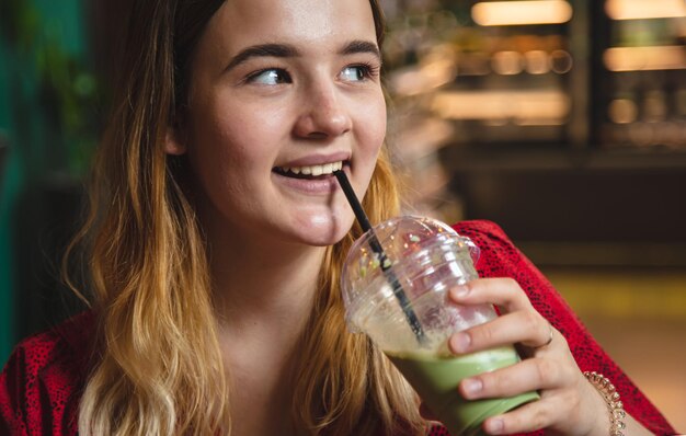 Une jeune femme dans un café boit une boisson verte au lait glacé