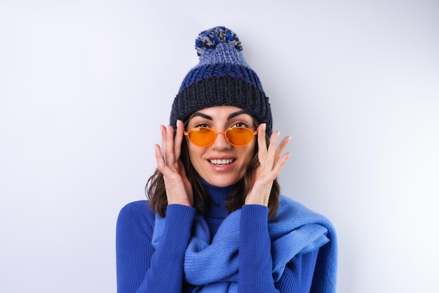 Jeune femme dans un chapeau à col roulé de golf bleu et des lunettes de soleil écharpe sur un fond blanc joyeux de bonne humeur