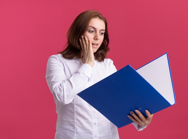 Jeune femme, dans, chemise blanche, tenue, dossier, regarder, étonné, et, surpris, debout, sur, mur rose