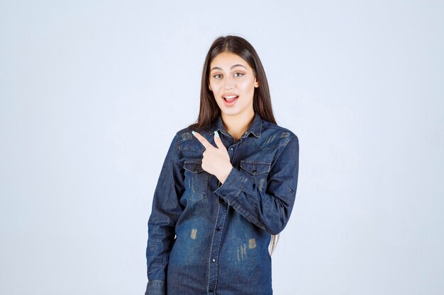 Jeune femme dans une chemise en jean pointant vers la gauche avec les émotions du visage