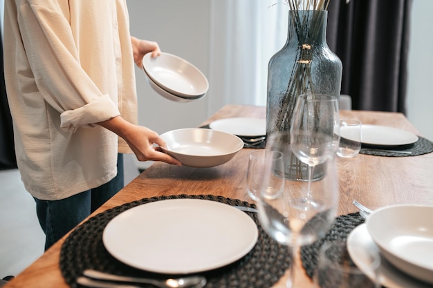 Jeune femme dans une chemise swhite mettant des assiettes sur la table