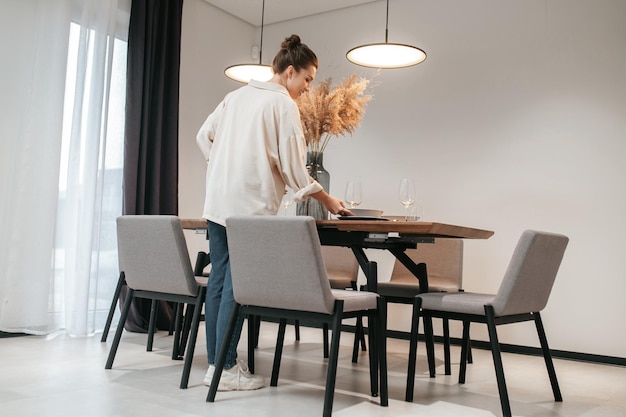 Jeune femme dans une chemise swhite mettant des assiettes sur la table