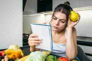 Photo gratuite une jeune femme dans la cuisine avec un carnet parmi les légumes