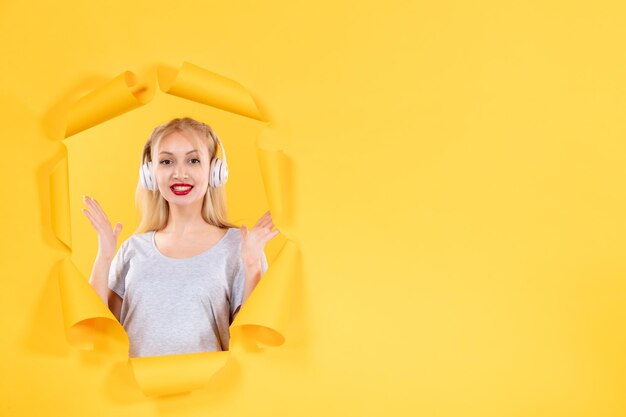 Jeune femme dans les écouteurs sur le son audio de la musique ultrasonore de fond de papier jaune déchiré