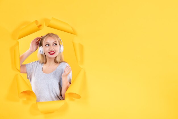 Jeune femme dans les écouteurs sur la surface du papier jaune déchiré