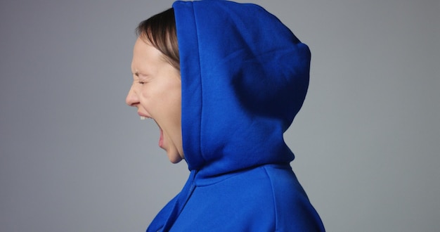 Jeune femme dans un grand sweat à capuche bleu vif sans étiquette crie et agit effrayé et en colère montrant le stress